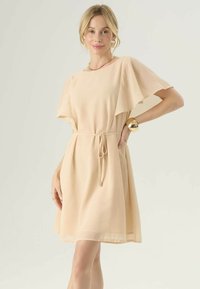 Abito a maniche corte, lungo fino al ginocchio, in chiffon nudo con vita regolabile. Presenta una silhouette rilassata e una texture morbida e fluida.
