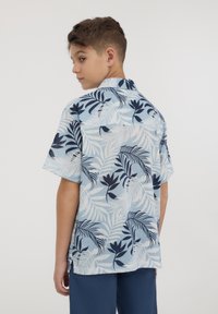 Camicia a maniche corte, blu chiaro con pattern a foglie blu navy, colletto con bottoni, vestibilità rilassata e dettaglio sullo yoke posteriore. Adatta per un abbigliamento casual.