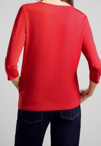 Rotes Langarmshirt mit rundem Halsausschnitt und weichem Material. Hat einen lässigen Schnitt, mit Dreiviertelärmeln und einem glatten Rücken.