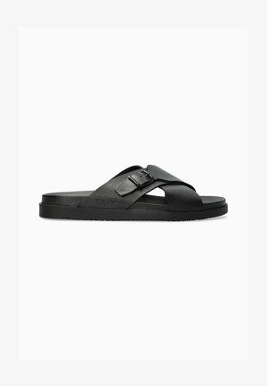 Sandale noire en cuir à enfiler avec des brides croisées, une boucle métallique et une semelle texturée, portant la marque "Mephisto" sur le côté.