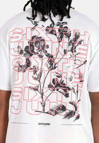 Wit T-shirt met een grote zwart-roze grafische tekstontwerp met "SIXTH JUNE" en bloemenpatronen; korte mouwen, standaard pasvorm.
