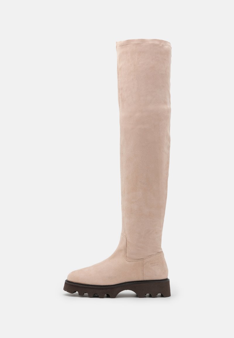 Beige Wildlederstiefel bis zum Knie mit einem eleganten Design, runder Zehenform und dicker brauner Gummisohle, die über strukturierte Rillen für besseren Halt verfügt.