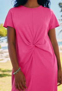 Robe en coton rose à manches courtes avec un design torsadé sur le devant et une coupe décontractée. Texture lisse, longueur mi-cuisse, style décontracté.