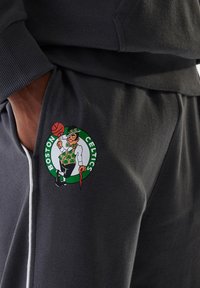 Gray sweatpants featuring a Boston Celtics logo. The design includes a cartoon leprechaun holding a basketball and an umbrella.