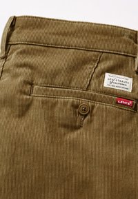 Pantalones de pana marrones con textura de estrías verticales, con cierre de botón y una etiqueta de Levi's en el bolsillo trasero.