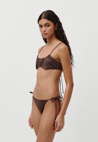 Brown bikini set featuring a gathered top with thin straps and side-tie bottoms, made from smooth, stretchy fabric with minimal detailing.