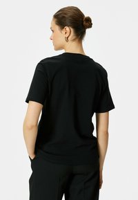 Sort bomulds t-shirt med korte ærmer, rund hals og en afslappet pasform, vist fra ryggen, parret med skræddersyede sorte bukser.