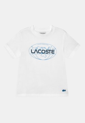 Camiseta blanca de algodón con un gráfico de un globo azul y el texto "LACOSTE" en negro. Un pequeño logo de cocodrilo azul está bordado en el dobladillo.