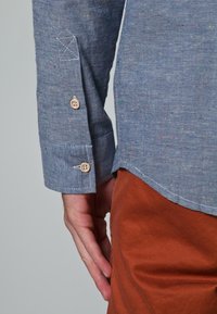 Camisa azul con botones, estampada con motas, puño con costura y dos botones. Tela texturizada con motas de colores y dobladillo recto.