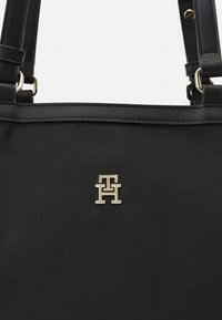 Schwarze Nylon-Shopper-Tasche mit goldfarbener metallic Logo-Akzent. Das Design umfasst doppelte Griffe und eine glatte, strukturierte Oberfläche.