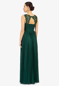 Langes grünes Kleid mit einem plissierten Rock, Spitzenakzenten am Rücken und einem gerafften Oberteil, das ein Ausschnittdesign im Nackenbereich aufweist.
