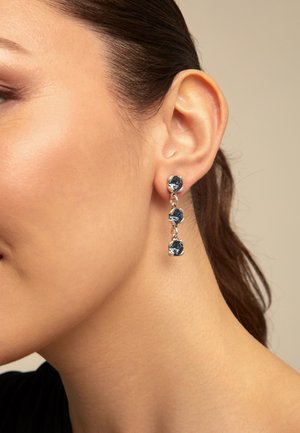Boucles d'oreilles en argent suspendues avec trois pierres bleues, présentant un design circulaire et une texture lisse, sur un fond neutre.