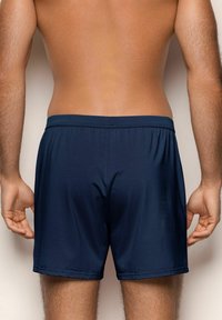 Námorně modré plavky s elastickým pasem, hladkou texturou a délkou nad kolena. Žádné viditelné vzory ani kovové detaily.