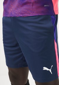 Calções atléticos azul marinho com acentos laterais em rosa. Feitos de material leve, apresentam um logótipo branco da Puma na perna esquerda.
