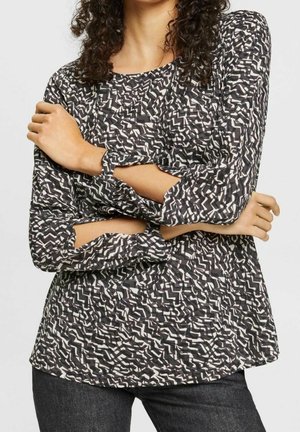 Top a fantasia in bianco e nero con maniche lunghe e ritagli, scollatura rotonda e vestibilità ampia, realizzato in un tessuto leggero.