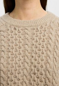 Suéter tejido beige con un patrón de punto de cable, cuello acanalado grueso y un acabado texturizado con un aspecto suave.
