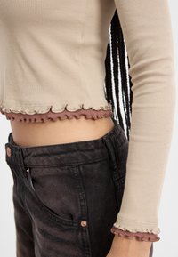 Kreminė juostuota trumpa palaidinė su rožine banguota apatine dalimi; derinama su juodomis džinsinėmis kelnėmis aukštu liemeniu, turinčiomis vario spalvos mygtukų detales ir lygiu paviršiumi.