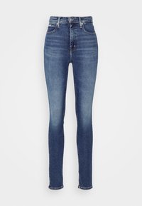 Džíny s vysokým pasem v tmavě modrém denimu, které mají štíhlý siluetu, mírné zesvětlení a tradiční pětikapsový design.