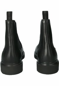 Botas de tobillo de cuero negro que presentan una textura suave, paneles laterales elásticos y una suela de goma baja y resistente. Tiradores en la parte posterior para facilitar el uso.