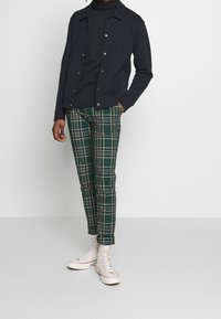 Černá saková bunda, fitted zelené kostkované kalhoty s bílými akcenty, doplněné bílými vysokými teniskami. Hladká tkanina a slim fit.