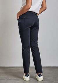 Pantalones ajustados azul marino con bolsillos traseros, hechos de una tela suave; usados con zapatillas blancas. Costuras visibles y un sutil detalle de marca.