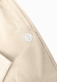 Beige sweatshirt met een zachte textuur, capuchon en een witte geborduurde logo op de borst. Rechte snit met zichtbare stikdetails.
