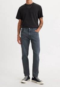 Svart bomullströja, grå denimjeans och svarta canvas sneakers. Jeanserna har en klassisk passform med en blekt finish och metalldetaljer.