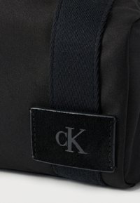 Μαύρη υφασμάτινη τσάντα με κομψό σχεδιασμό, υφή στο λουρί και μαύρο βελούδινο πλαίσιο με ανάγλυφο λογότυπο «cK».