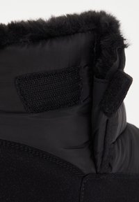 Schwarze gefütterte Stiefel mit einem von Fell gesäumten Kragen, glattem Stoff und einem strukturierten Klettverschluss. Schlankes Design mit dezenten Nähten.