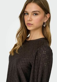 Braune Bluse mit einem strukturierten, bestickten Muster. Verfügt über einen runden Ausschnitt und gepuffte Ärmel, die eine sanfte Silhouette kreieren.