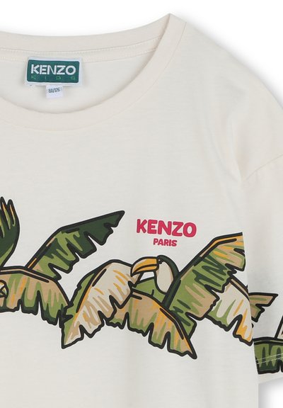 T-shirt en coton couleur crème ornée de feuilles de palmier vertes et jaunes et d'un graphisme d'oiseau, avec "KENZO PARIS" en texte rose vif.