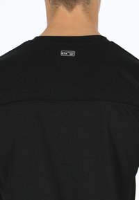 Musta urheilupaita, jossa on pyöreä kaula-aukko, teksturoitu kangas ja STX Quick Dry -merkki takana kaula-aukon lähellä.