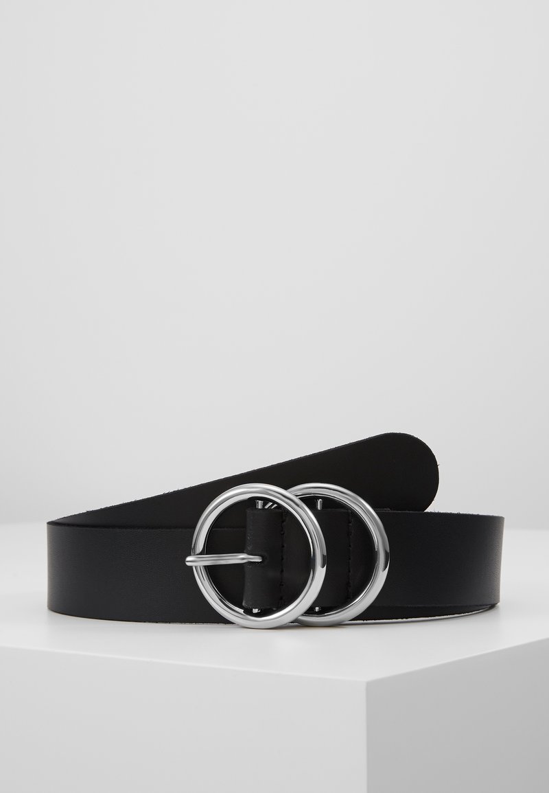 Ceinture en cuir noir avec boucle métallique argentée double ronde reposant sur une surface blanche sur fond gris uni.
