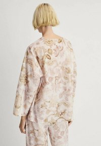 T-shirt à manches longues en tissu doux et léger avec un motif floral rose pâle et beige, présentant un col large et une coupe décontractée.