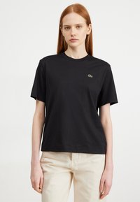 Schwarzes Baumwoll-T-Shirt mit Rundhalsausschnitt, kurzen Ärmeln und einem grünen gestickten Krokodil-Logo auf der linken Brust.