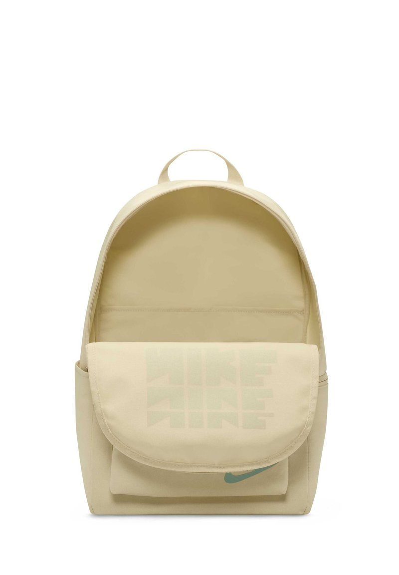 Mochila de color crema con un bolsillo en la solapa frontal que presenta un diseño gráfico de texto sutil y un acento de logo en color teal. Material de lona suave.