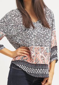 Blusa holgada con un patrón floral en blanco y negro, que presenta un dobladillo de paisley en melocotón y azul, y un borde texturizado negro.
