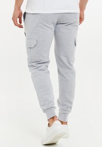 Grå cargo-joggers i mjukt tyg med sidofickor, elastiska muddar och en figursydd design. Bärs med vita sneakers.