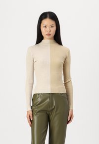 Turtleneck džemper s rebrastim uzorkom u dvije nijanse bež boje, uskog kroja. Uparen s hlačama od maslinaste zelene kože visokog struka, glatke teksture.