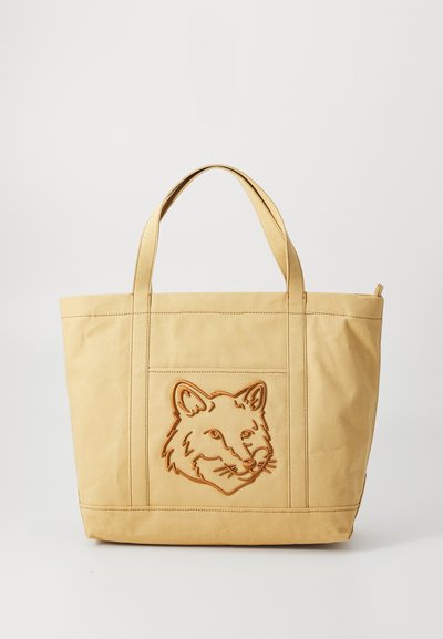 Yellow canvas tote bag featuring an embossed fox head design. Structured shape with two top handles, stitching detail, and zip closure.