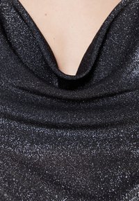 Tessuto nero con collo a cappa, dalla superficie scintillante e testurizzata, che riflette la luce. Il design presenta un scollo drappeggiato e una finitura liscia.