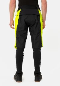 Zwarte en neongele shorts met een reguliere pasvorm, voorzien van ritszakken en een verstelbare tailleband, gecombineerd met zwarte leggings en schoenen.