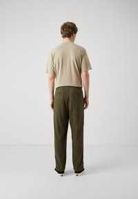 Beige katoenen t-shirt met korte mouwen, gecombineerd met olijfgroene, los zittende broeken met een elastische tailleband en een minimalistisch ontwerp.