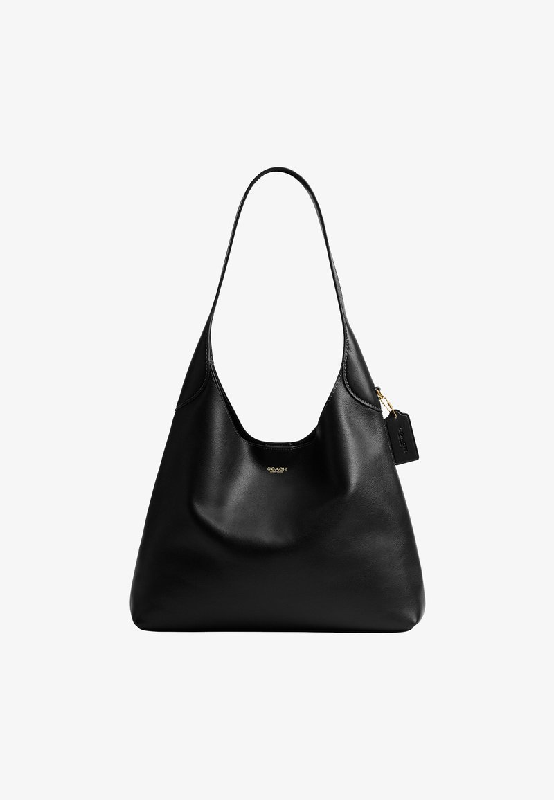 Sac à épaule Coach en cuir noir avec une seule bandoulière et un petit logo doré sur le devant, avec une étiquette en cuir attachée par une chaîne dorée.