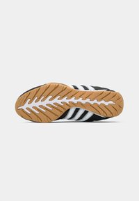 Sola de adidași Adidas alb-negru cu un model de striație în zigzag maro și alb, prezentată pe un fundal alb.