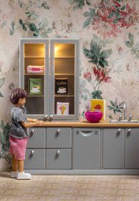 Set da cucina in plastica con armadietti grigi, piano di lavoro in legno, ciotola rosa e display illuminato contenente articoli vari a tema cibo colorati.