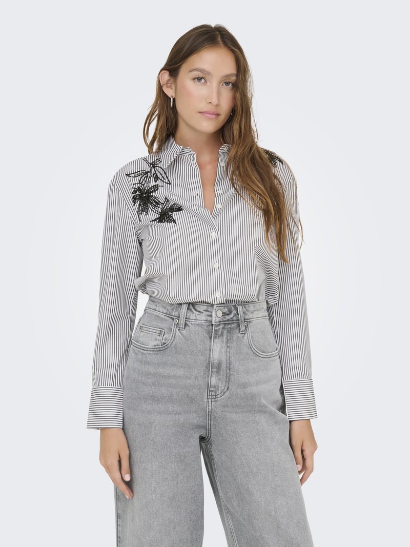 Camicia a righe con ricami floreali neri sulla spalla; abbinata a jeans in denim grigi a vita alta.
