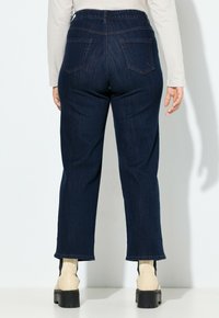 Jeans de mezclilla azul oscuro con una cintura alta, banda elástica en la cintura y piernas rectas. Presenta dos bolsillos traseros y un detalle de dobladillo sin terminar.