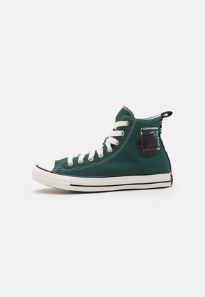 Wysoki zielony ciemny sneaker Converse z białymi sznurowadłami, białą gumową podeszwą, czarnym okrągłym logo i czarną pętlą na jednolitym tle.