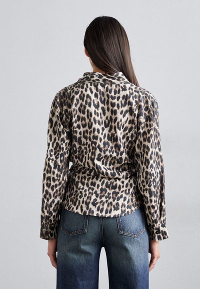 Camicia con stampa leopardata beige e nera, dal taglio morbido, con colletto e polsini abbottonati, abbinata a jeans in denim blu a vita alta.